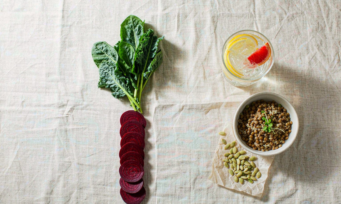 Overhead flat lay of beet, leafy greens, lentils, seeds and citrus water on linen