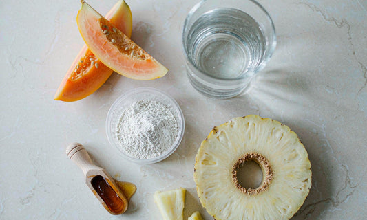Papaya, pineapple, enzyme powder and honey arranged on a pale marble countertop