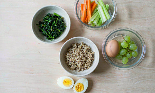 Overhead flat lay of simple meal prep components in bowls and glass containers on a pale wood table