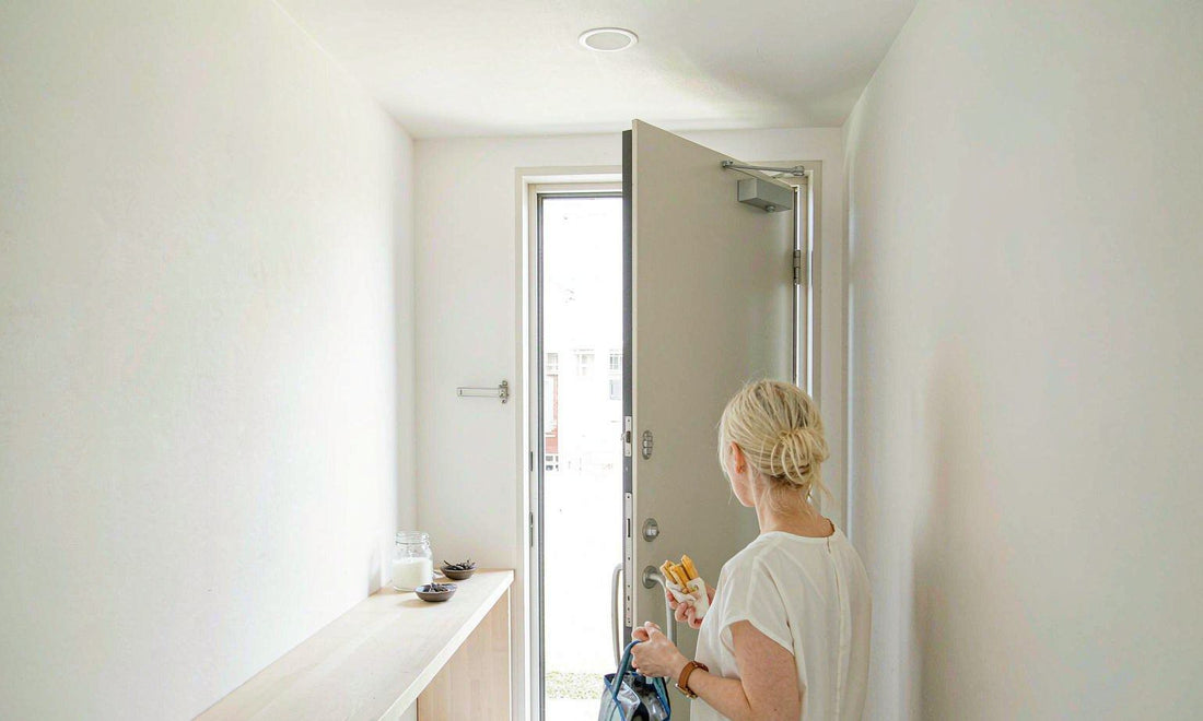 A person seen from behind in a bright entryway holding a lunch tote beside a jar of yogurt