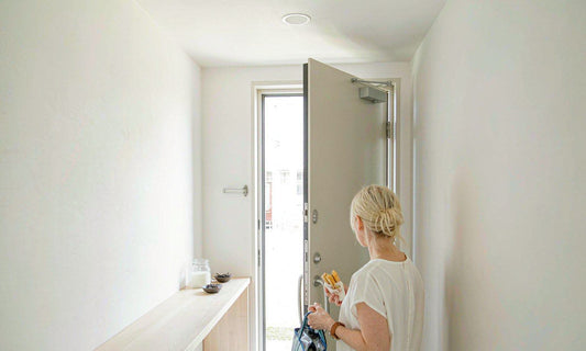 A person seen from behind in a bright entryway holding a lunch tote beside a jar of yogurt
