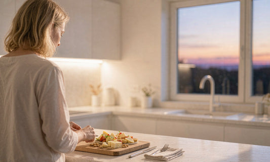 A woman seen from behind preparing a light evening snack in a warm kitchen at dusk.