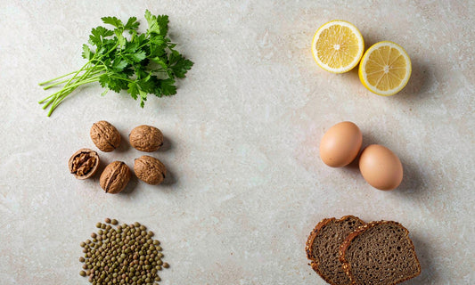 Overhead flat lay of nutrient dense whole foods with parsley, lemon, walnuts, eggs, lentils and rye bread