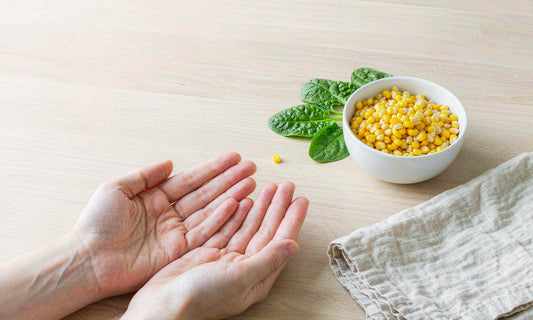 Pair of relaxed fair-skinned hands beside a bowl of corn kernels and fresh spinach leaves