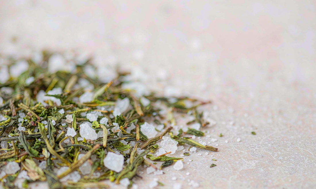 Macro view of green tea leaves and coarse white mineral crystals on a pale stone surface with soft bokeh
