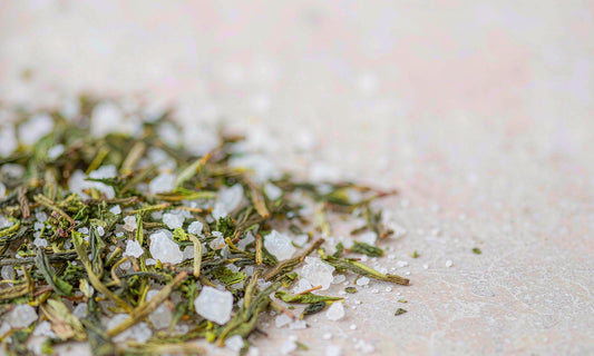 Macro view of green tea leaves and coarse white mineral crystals on a pale stone surface with soft bokeh