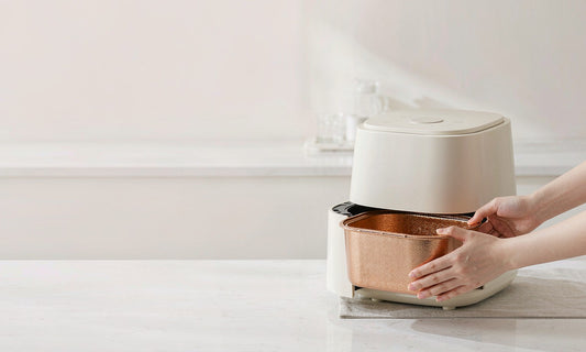 Hands sliding a golden basket into a modern white air fryer on a bright kitchen counter