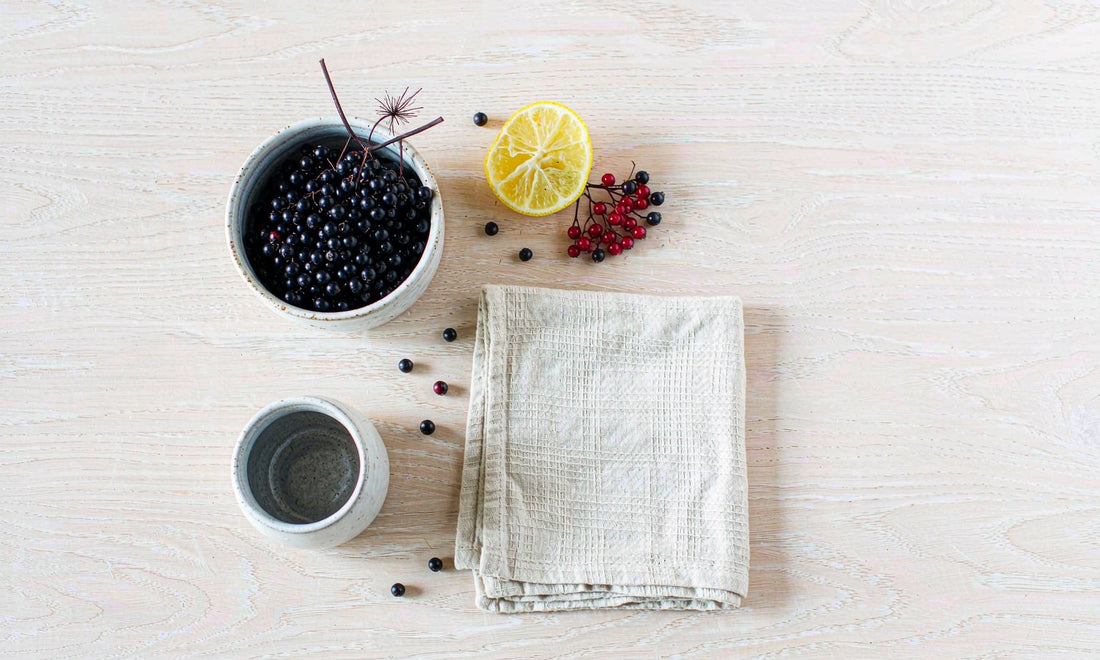 Overhead flat lay of elderberries, citrus and linen napkin on pale oak table