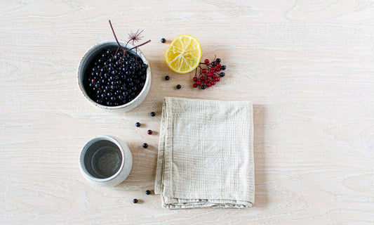 Overhead flat lay of elderberries, citrus and linen napkin on pale oak table