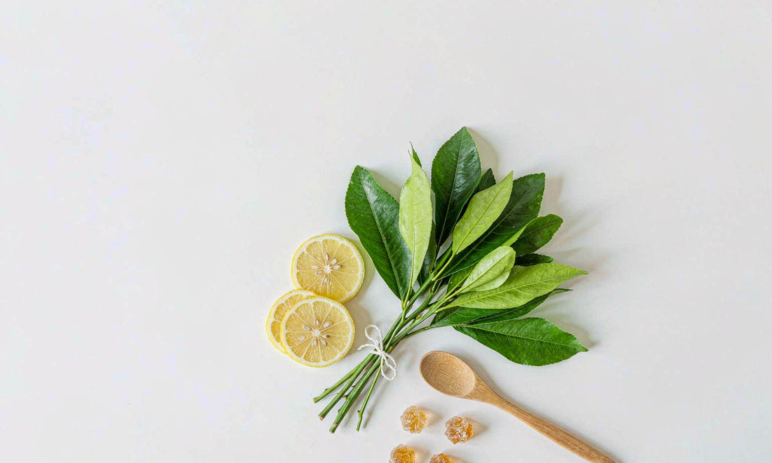 Top-down view of fresh green leaves, lemon slices and amber gummies on a clean surface, representing clean eating and liver support