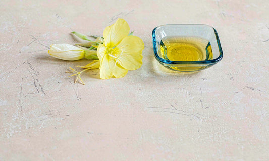 Evening primrose flowers beside a small glass dish of golden oil on a pale stone surface