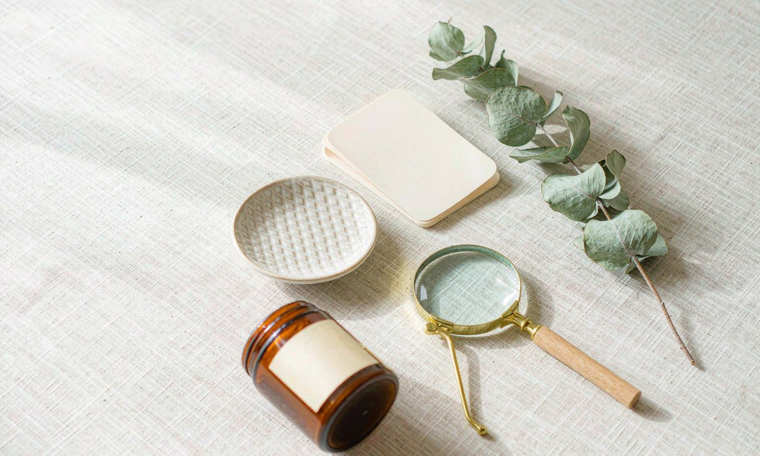 Overhead flat-lay of an amber jar, magnifying glass and blank card on pale linen for label reading