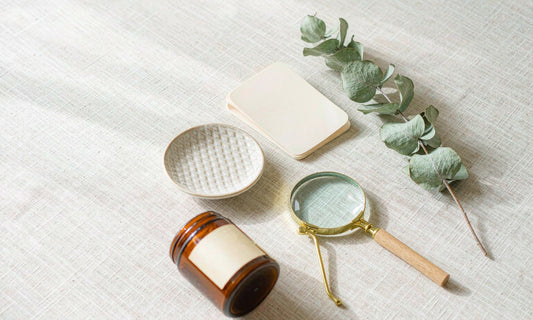 Overhead flat-lay of an amber jar, magnifying glass and blank card on pale linen for label reading