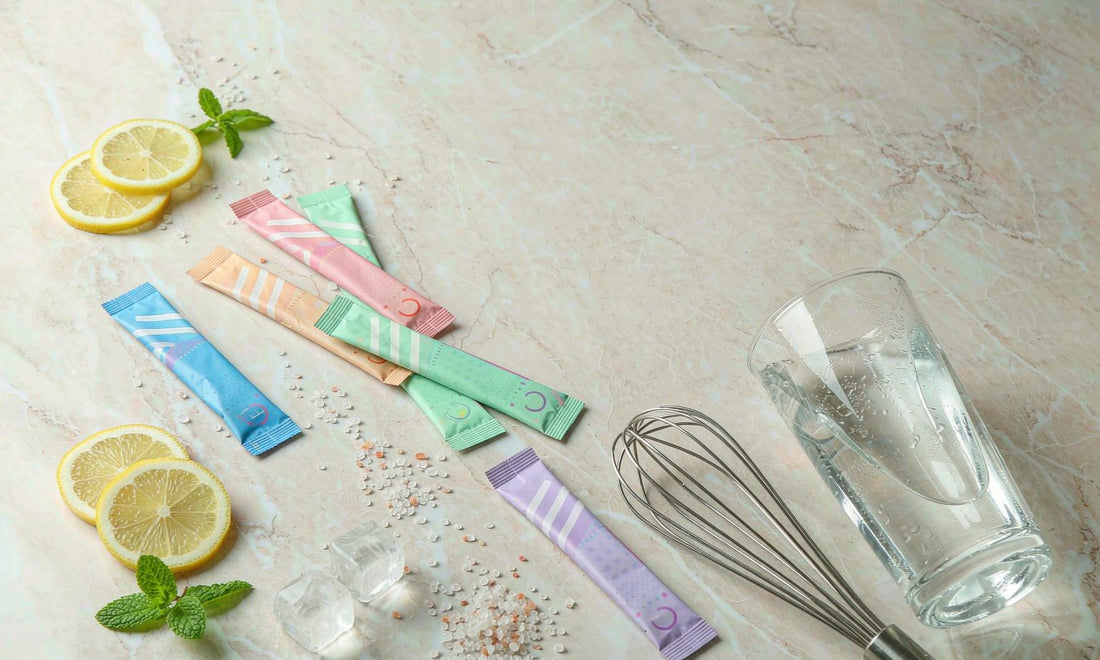 Colorful electrolyte drink powder sachets with lemon slices, mineral salts and a glass of water on marble