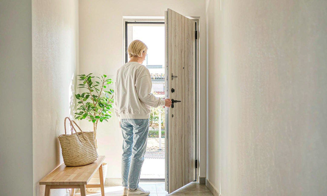 Person seen from behind opening a front door to let fresh air into a bright pale hallway