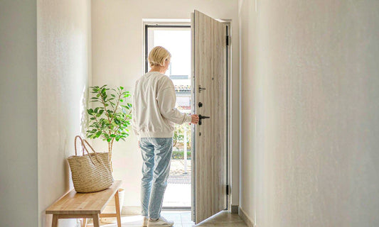 Person seen from behind opening a front door to let fresh air into a bright pale hallway