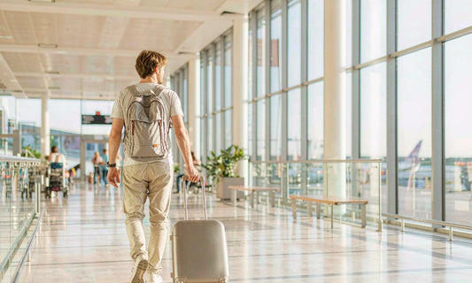 Traveler with a rolling suitcase seen from behind walking through a bright airport terminal at sunrise