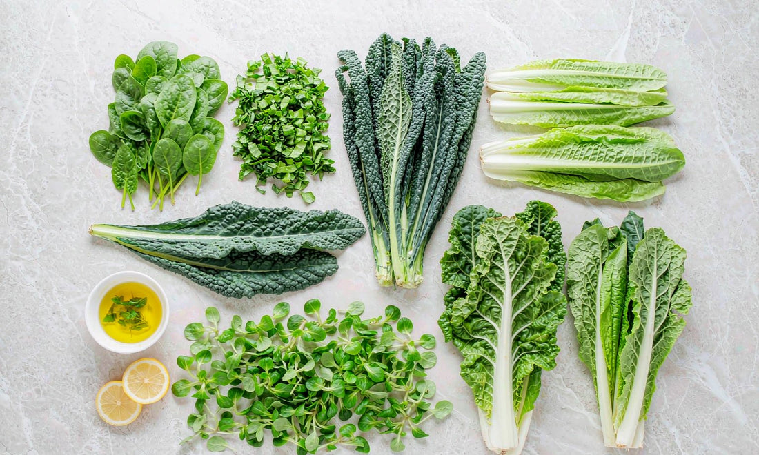 Overhead flat lay of spinach, kale, romaine and chard arranged neatly on a pale stone counter