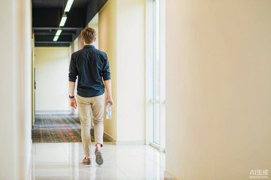 Man with light brown hair walking through a bright hallway carrying a clear water bottle