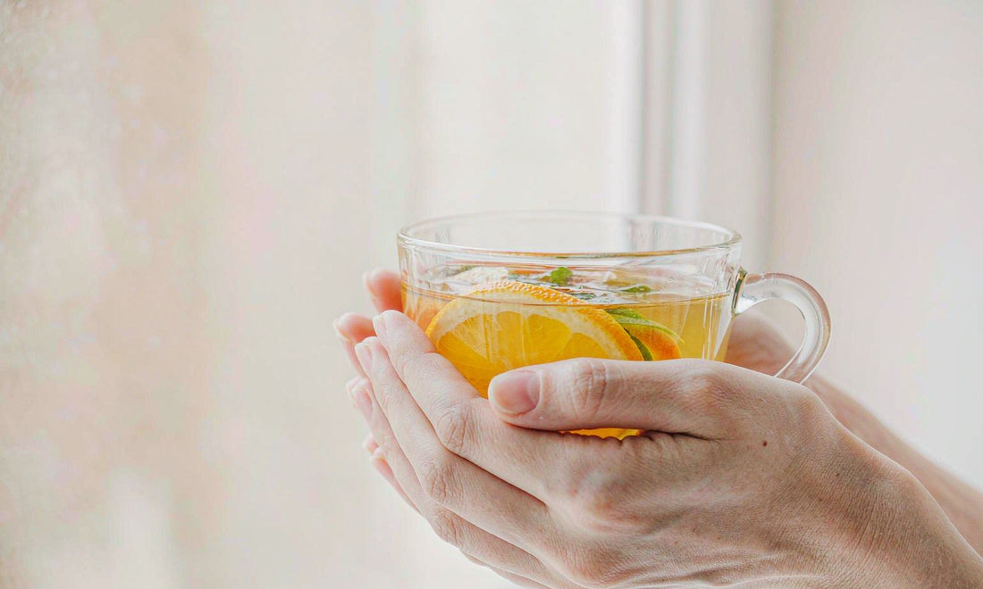 Hands cradling a warm mug of citrus tea with an orange slice, representing everyday immune support