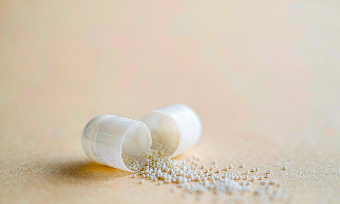 Macro view of smooth white capsules spilling fine granules across a pale matte surface