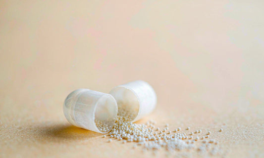 Macro view of smooth white capsules spilling fine granules across a pale matte surface