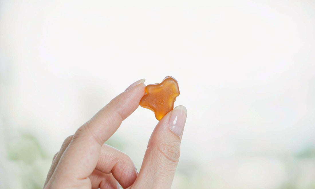 Hand holding a soft amber gummy about to be taken, representing everyday wellness