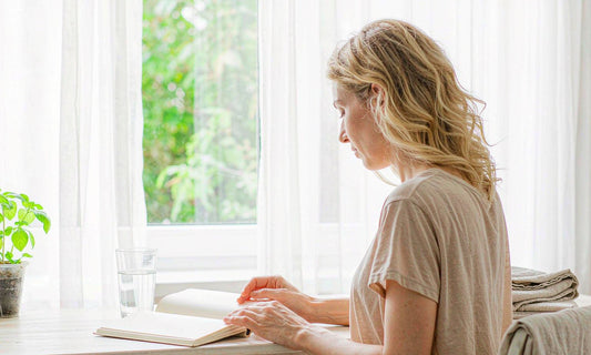 Woman planning a preconception wellness routine at a sunlit desk with notebook and glass of water