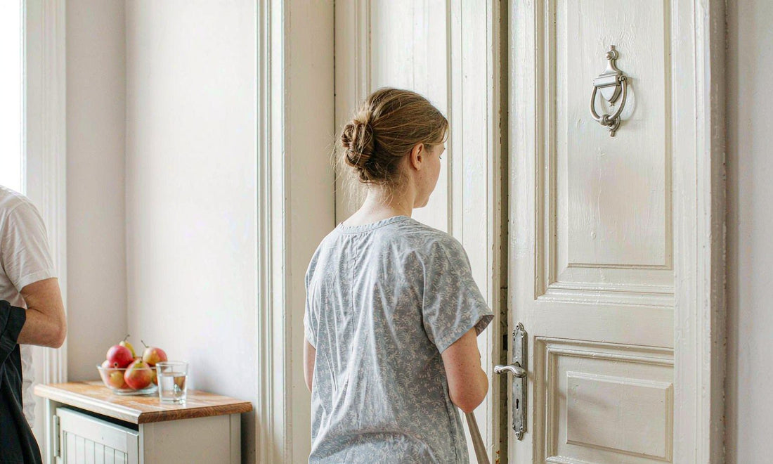 Person seen from behind reaching for a tote bag by a bright entryway door in the morning