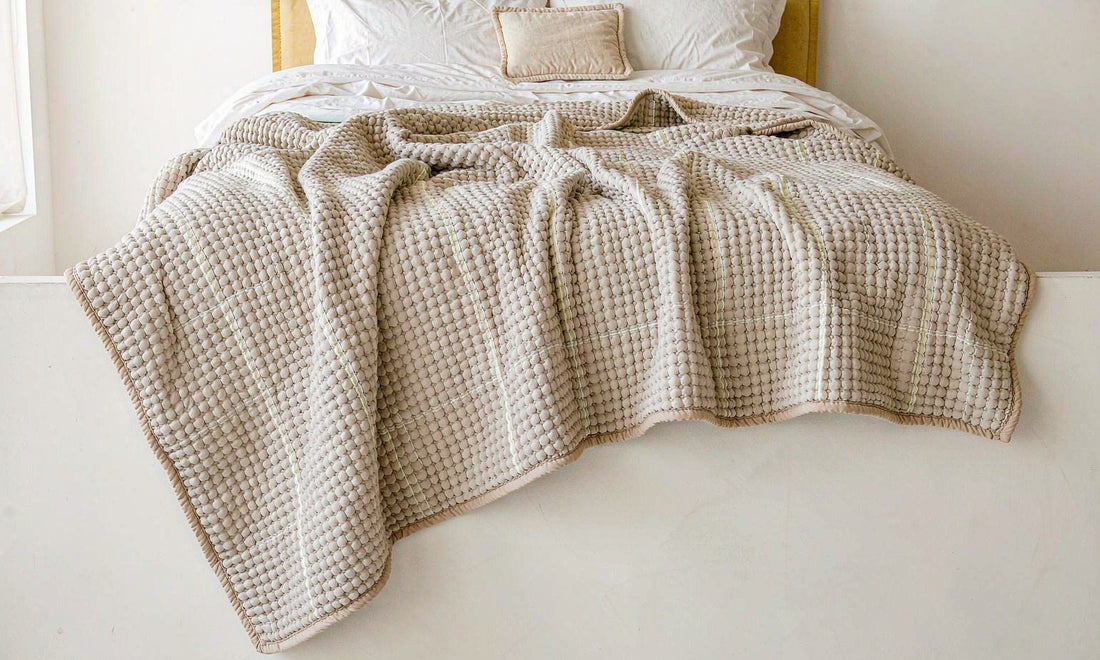 A chunky knit weighted blanket draped over a neatly made bed in soft natural daylight