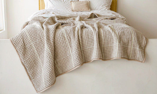 A chunky knit weighted blanket draped over a neatly made bed in soft natural daylight