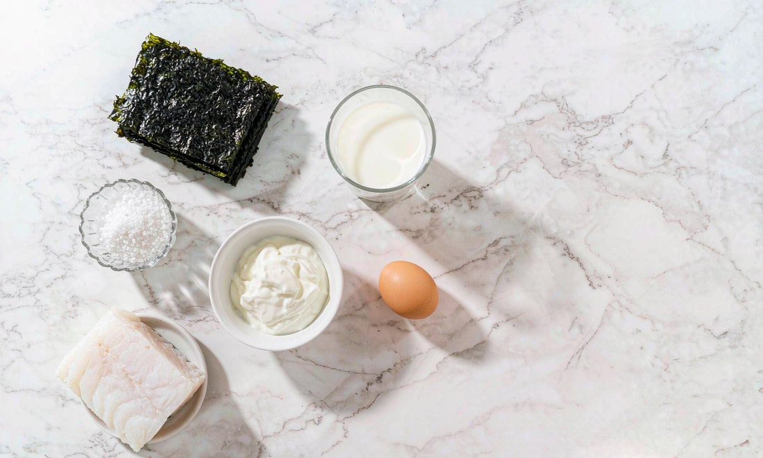 Overhead flat lay of iodine rich foods: seaweed, white fish, milk, yogurt, egg and salt.