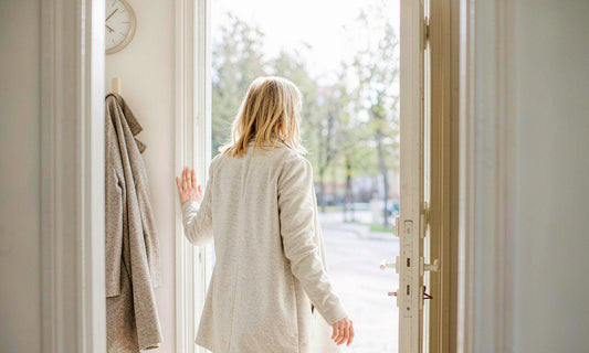 A person in a light coat stepping out of a bright entryway into crisp early morning daylight