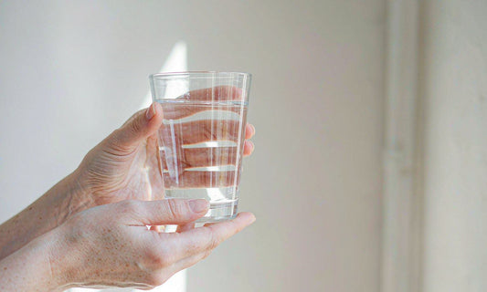 Hands holding a clear glass of water in soft sunlight, representing daily circulation support