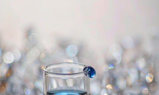 Macro close up of deep sapphire blue liquid droplet on a glass vial rim with soft bokeh crystals