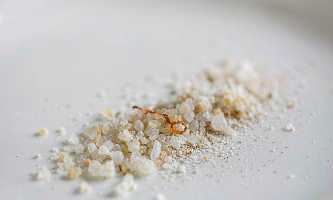 Macro close-up of pale sea salt crystals with a curl of dried seaweed on white ceramic
