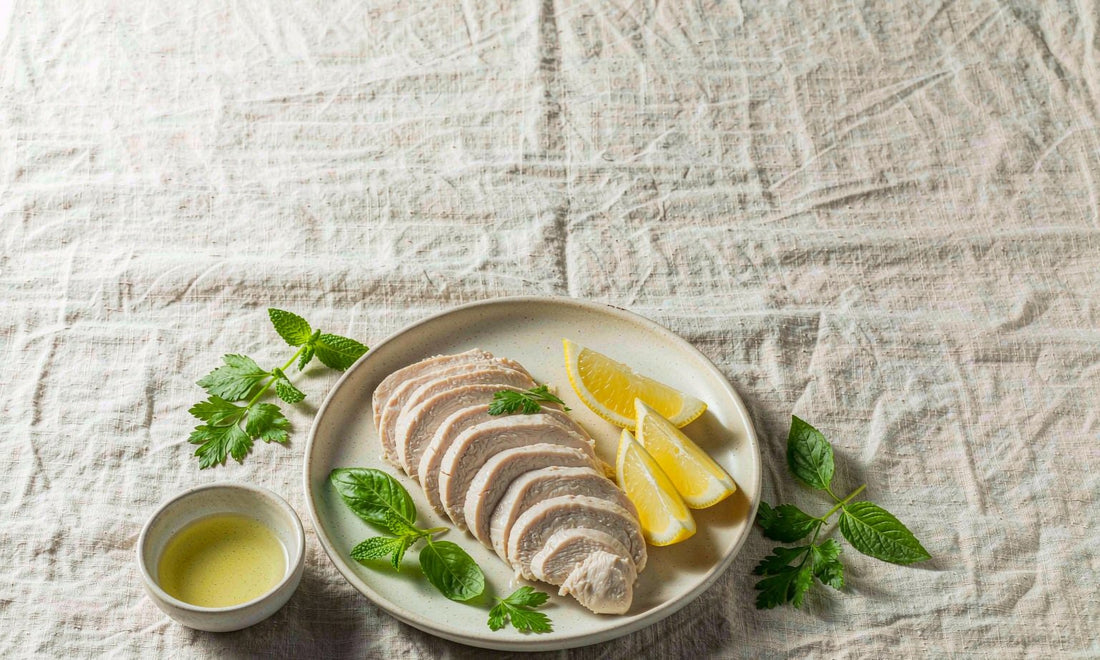 Top down flat lay of sliced chicken breast with lemon and fresh herbs on a linen cloth