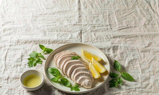 Top down flat lay of sliced chicken breast with lemon and fresh herbs on a linen cloth