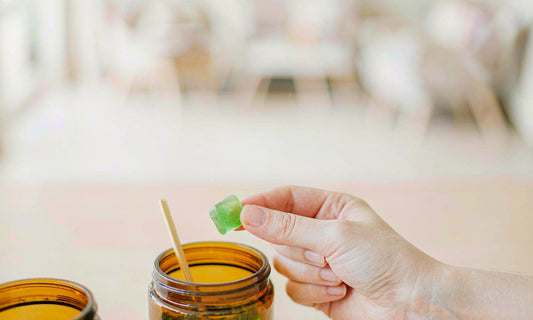 Hand lifting a green gummy from an amber jar on a bright breakfast table in soft morning light