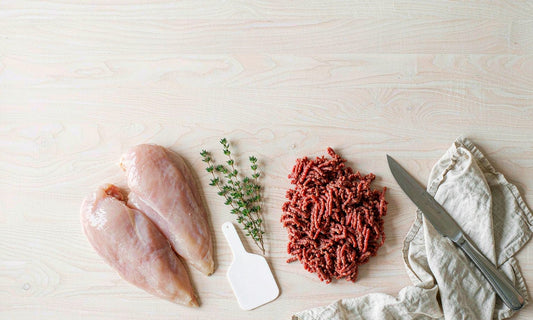 Raw chicken breast and grass fed beef mince side by side on a pale board with thyme, knife and linen napkin