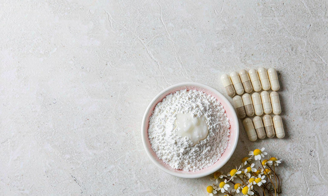 White mineral powder and capsules arranged beside chamomile flowers on a stone surface