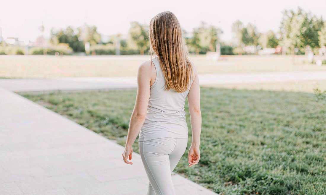 Woman in gray athletic wear seen from behind walking along a sunlit park path in early morning