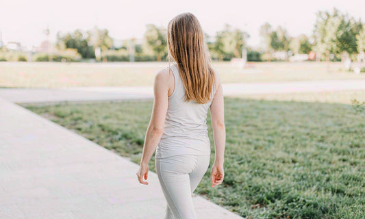 Woman in gray athletic wear seen from behind walking along a sunlit park path in early morning