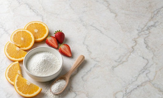 Bowl of fine white collagen peptide powder with a wooden scoop beside fresh orange slices