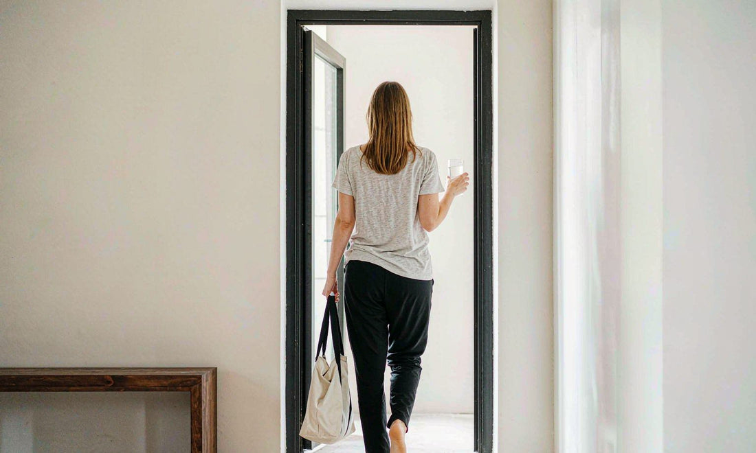 Person with light skin seen from behind walking through a bright minimalist entryway with a tote bag