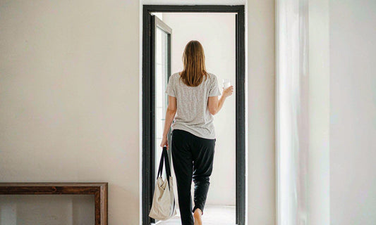Person with light skin seen from behind walking through a bright minimalist entryway with a tote bag