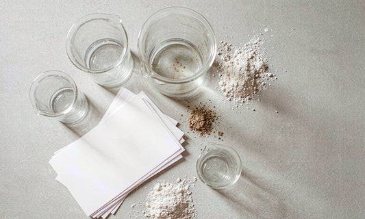 Glass beakers, blank papers and fine powder arranged on a pale surface for quality testing