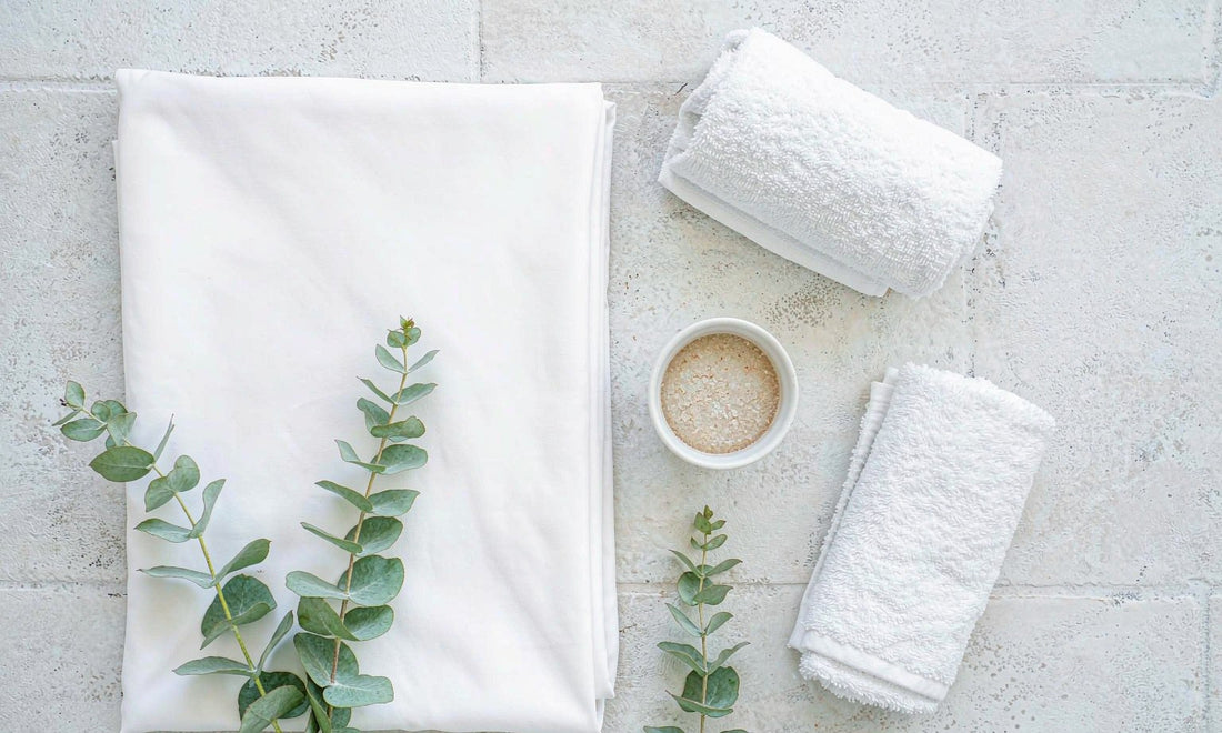 Rolled white spa towels and eucalyptus sprigs arranged in a calm grid on pale stone