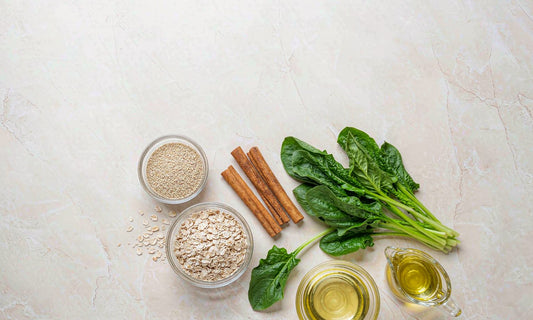 Ingredient flat lay of leafy greens, oats, quinoa and cinnamon on pale stone