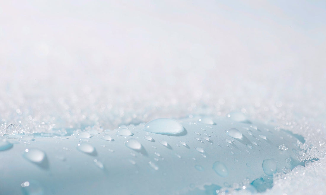 Extreme macro of clear water droplets beading on a cool pale blue ceramic surface with crystalline salt edges